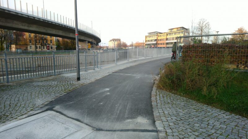 Radweg, links Gitter, rechts Bänke