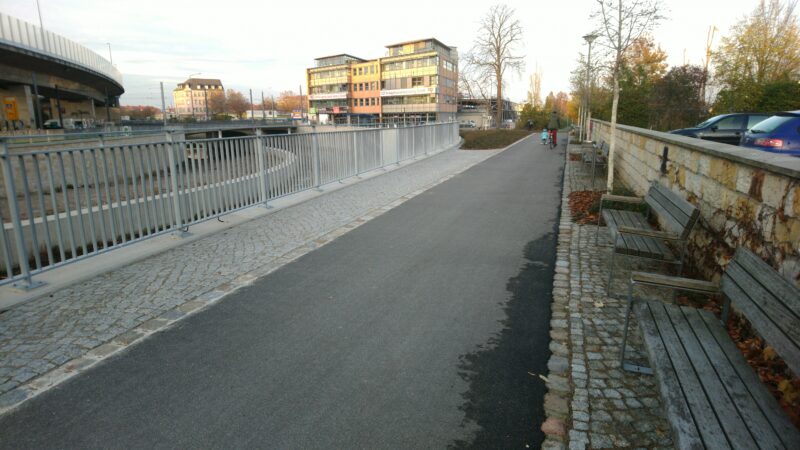 Radweg, links Gitter, rechts Bänke