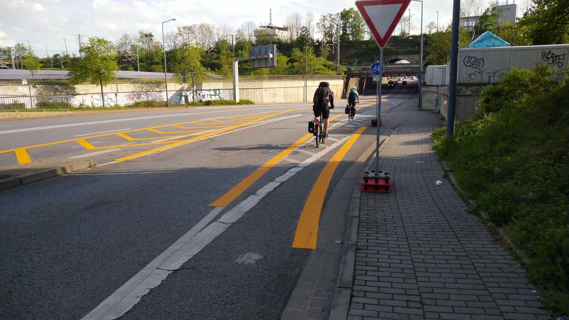 Straße mit vielen gelben Markierungen, zwei Radfahrer von hinten, keine Autos