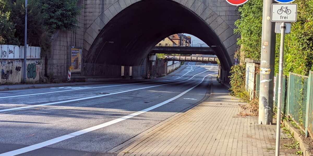 Straße mit mehreren Spuren (Bus-Spur, zwei Fahrspuren, ein Radweg), daneben ein Fußweg, freigegeben für Radfahrer. Kein Fahrzeug ist zu sehen.