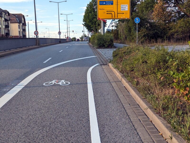 Straße mit einer Fahrspur und einem Radweg, der nach rechts auf den Rad und Fußweg abbiegt. Kein Fahrzeug auf dem Bild.